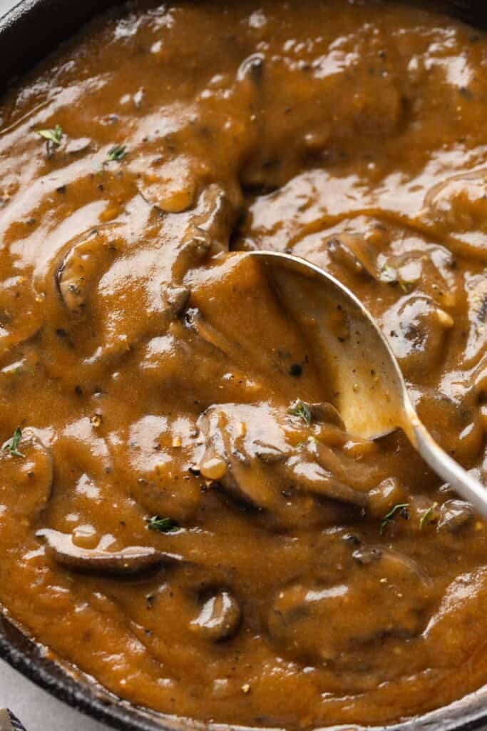 A spoon stirring mushroom gravy in a cast iron pan