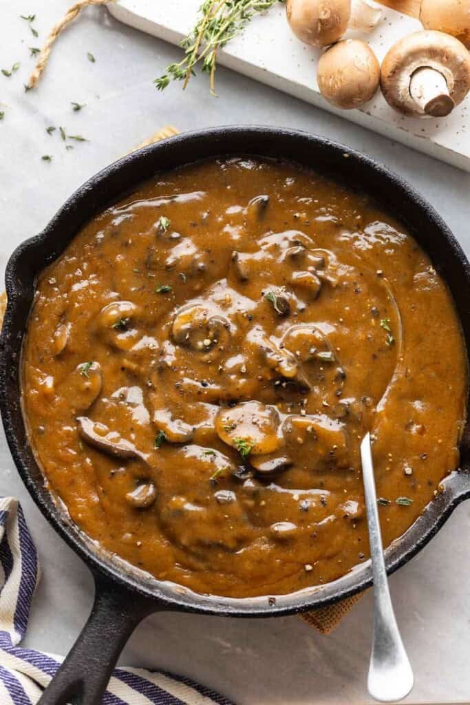 A cast iron pan full of mushroom gravy with fresh thyme leaves sprinkled on top