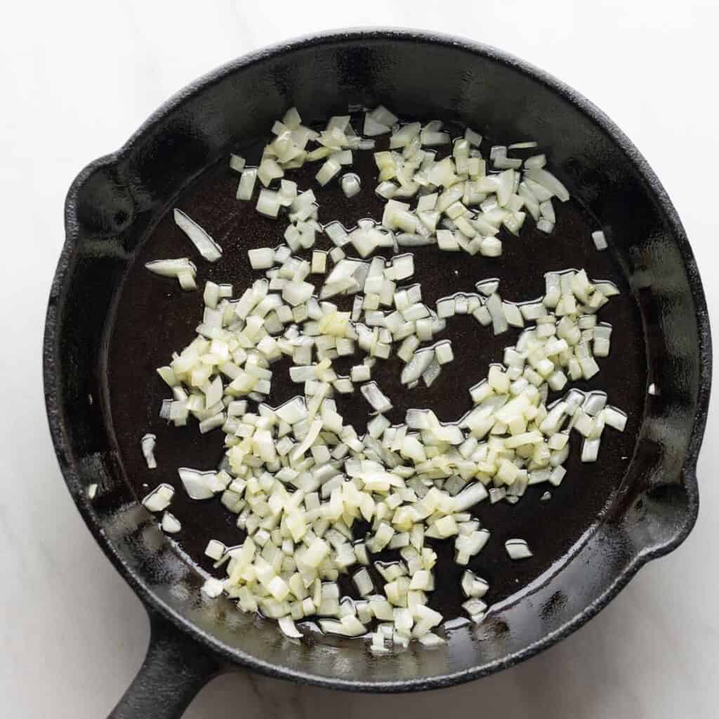 diced onions sautรฉing in a cast iron pan