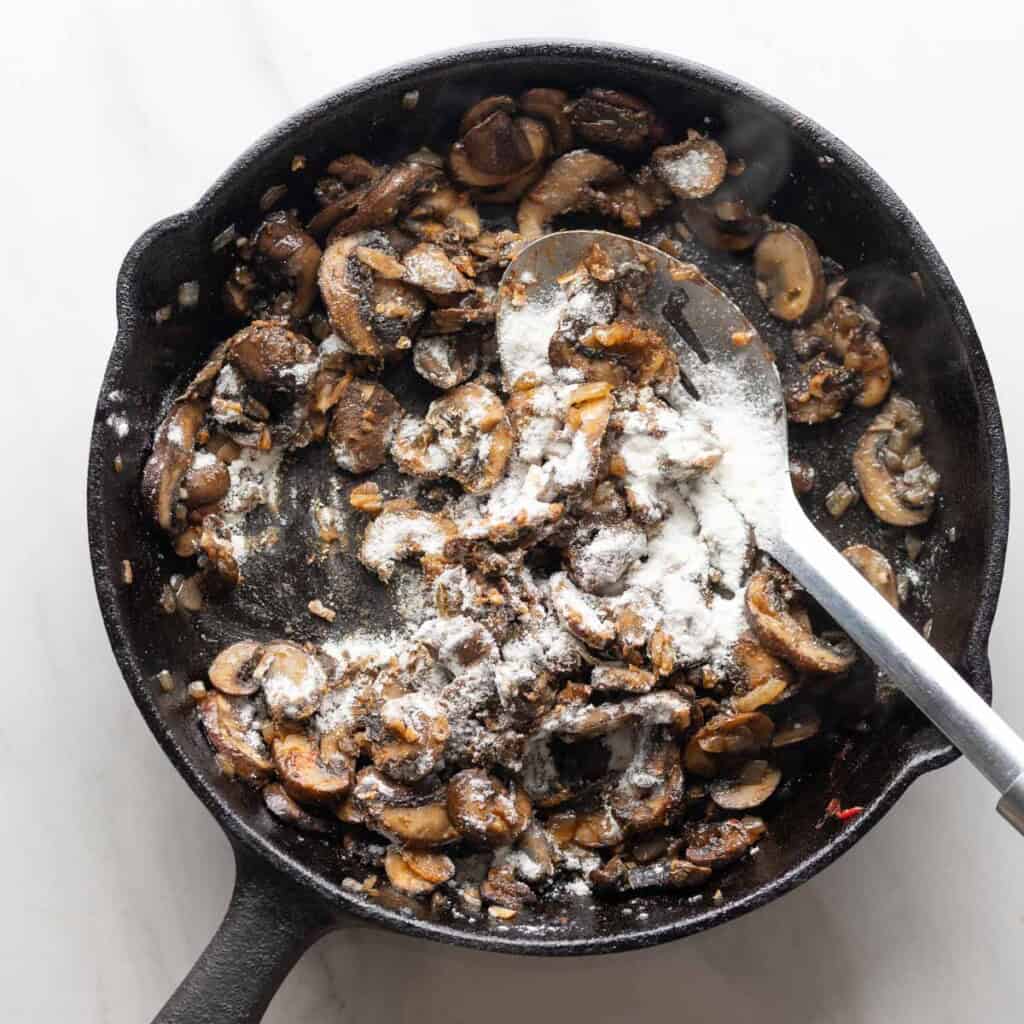 gluten free flour sprinkled over sautรฉd mushrooms and in a cast iron pan