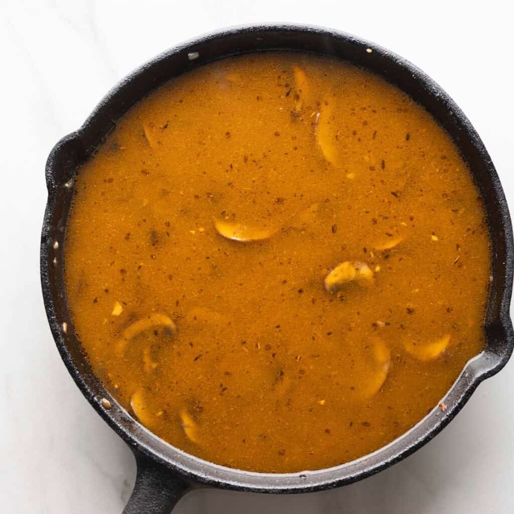 a cast iron pan in the process of making mushroom gravy before it thickens up