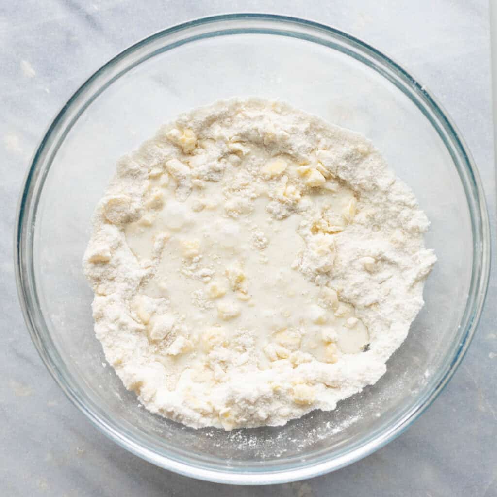 buttermilk added to a mixing bowl full of whisked dry ingredients and cold butter bits