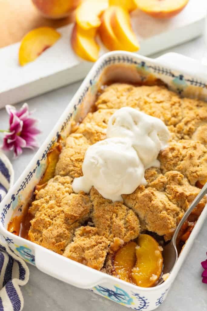 Gluten free peach cobbler with vanilla ice cream on top in a baking dish