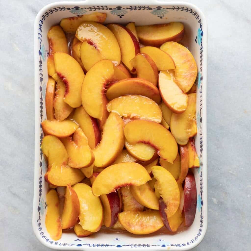sliced peaches macerating in a baking dish