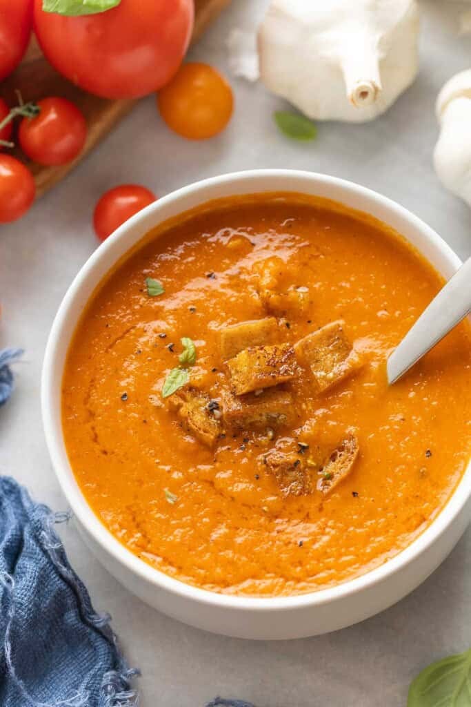 A bowl of roasted tomato soup with gluten free croutons and a few small leaves of fresh basil.