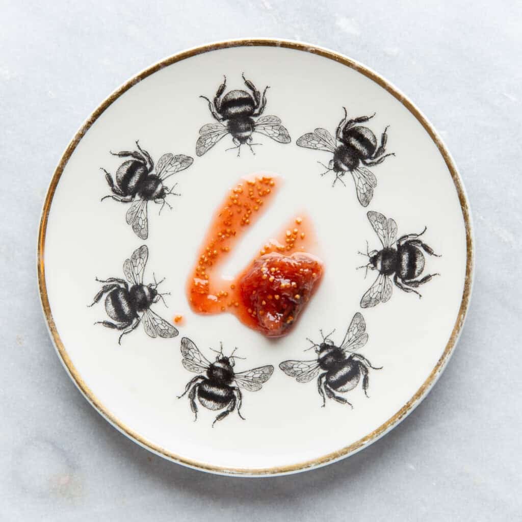 A small, chilled plate with a spoonful of fig jam in the middle showing a line through the middle of the jam. The line in the middle demonstrates that the jam has cooked and thickened enough to be done.