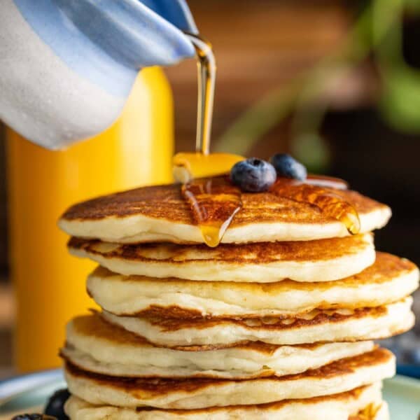 A stack of gluten free pancakes with maple syrup pouring on top
