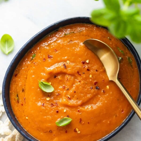 A bowl of roasted tomato soup with fresh basil leaves and red chili flakes sprinkles on top