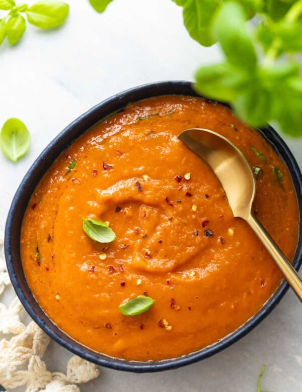A bowl of roasted tomato soup with fresh basil leaves and red chili flakes sprinkles on top
