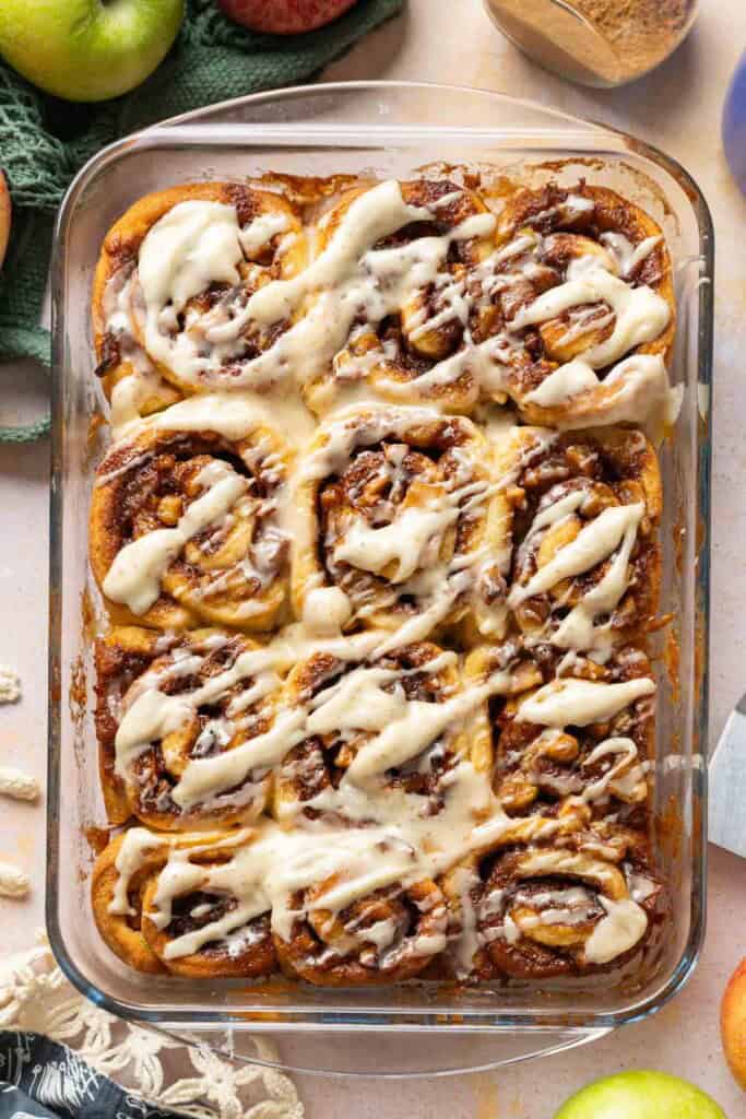 A 9x13 inch glass baking dish full of Gluten Free Apple Cinnamon Rolls with a brown butter cream cheese frosting drizzled over top.
