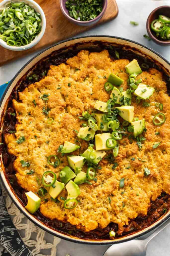 Gluten Free Chili Cornbread Casserole in a large dutch oven pan with diced avocado, spring onions and cilantro on top
