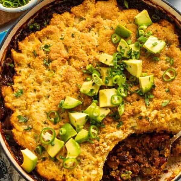 Gluten Free Chili Cornbread Casserole in a large dutch oven pan with diced avocado, spring onions and cilantro on top