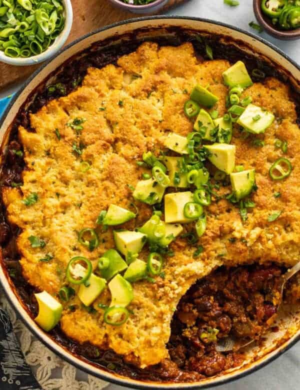 Gluten Free Chili Cornbread Casserole in a large dutch oven pan with diced avocado, spring onions and cilantro on top