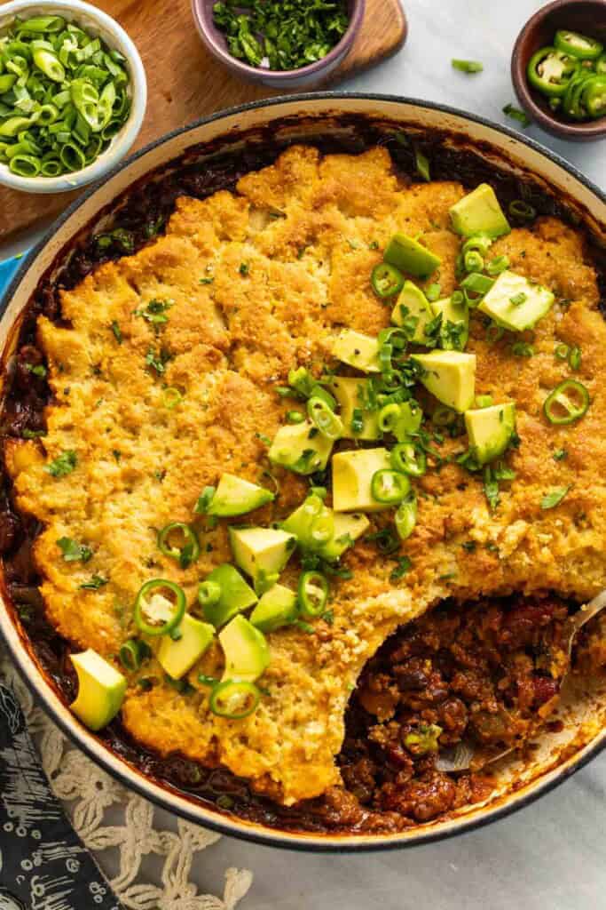 Gluten Free Chili Cornbread Casserole in a large dutch oven pan with diced avocado, spring onions and cilantro on top