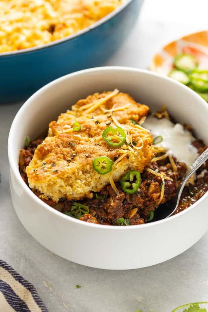 A bowl of chili with gluten free cornbread on top with sliced jalapenos