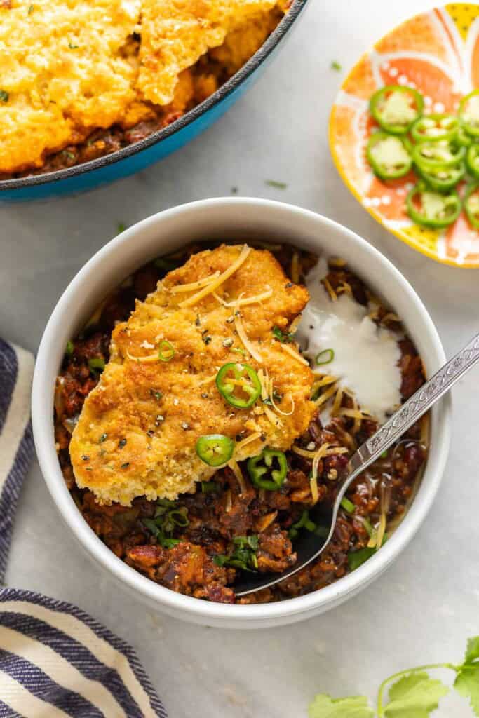 A bowl with a serving of Gluten Free Chili Cornbread Casserole garnished with sour cream and jalapeno slices.