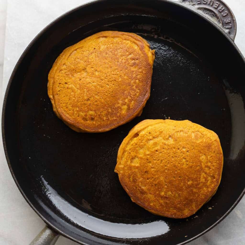 Two pumpkin pancakes in a cast iron skillet.